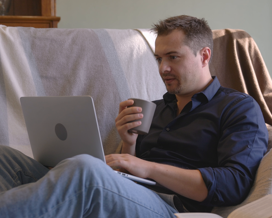 Tobias Meyknecht arbeitet vom Sofa aus am Laptop, Tasse in der Hand.